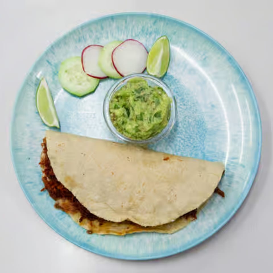 A Toortugas Mexican Torteria quesadilla with guacamole, cucumber, radish, and lime on a blue plate.