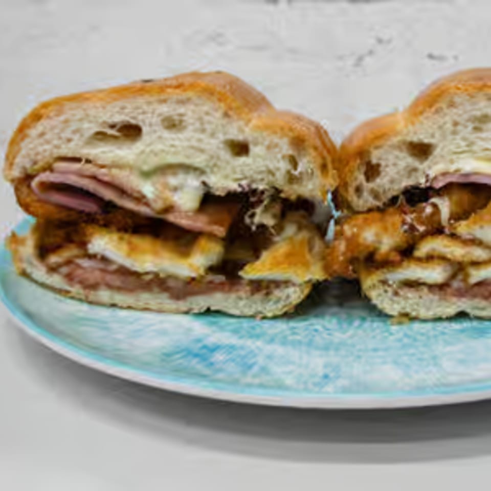 A Toortugas Mexican Torteria sandwich, cut in half, revealing layers of meat, cheese, and beans.