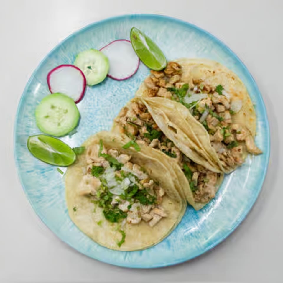 Three chicken tacos with cilantro and onions, served with lime, radish, and cucumber slices.