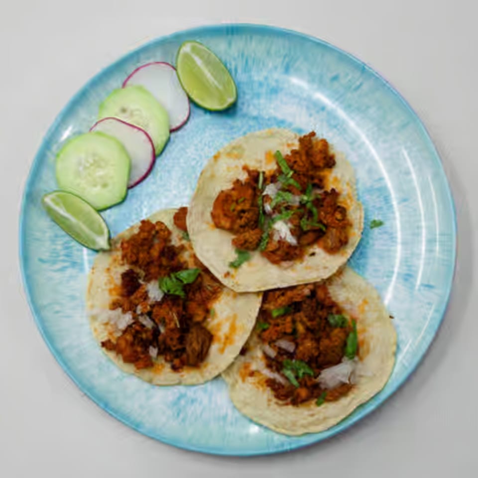 Three Toortugas Mexican Torteria tacos with meat, onions, cilantro, and a side of cucumber, radish, and lime.
